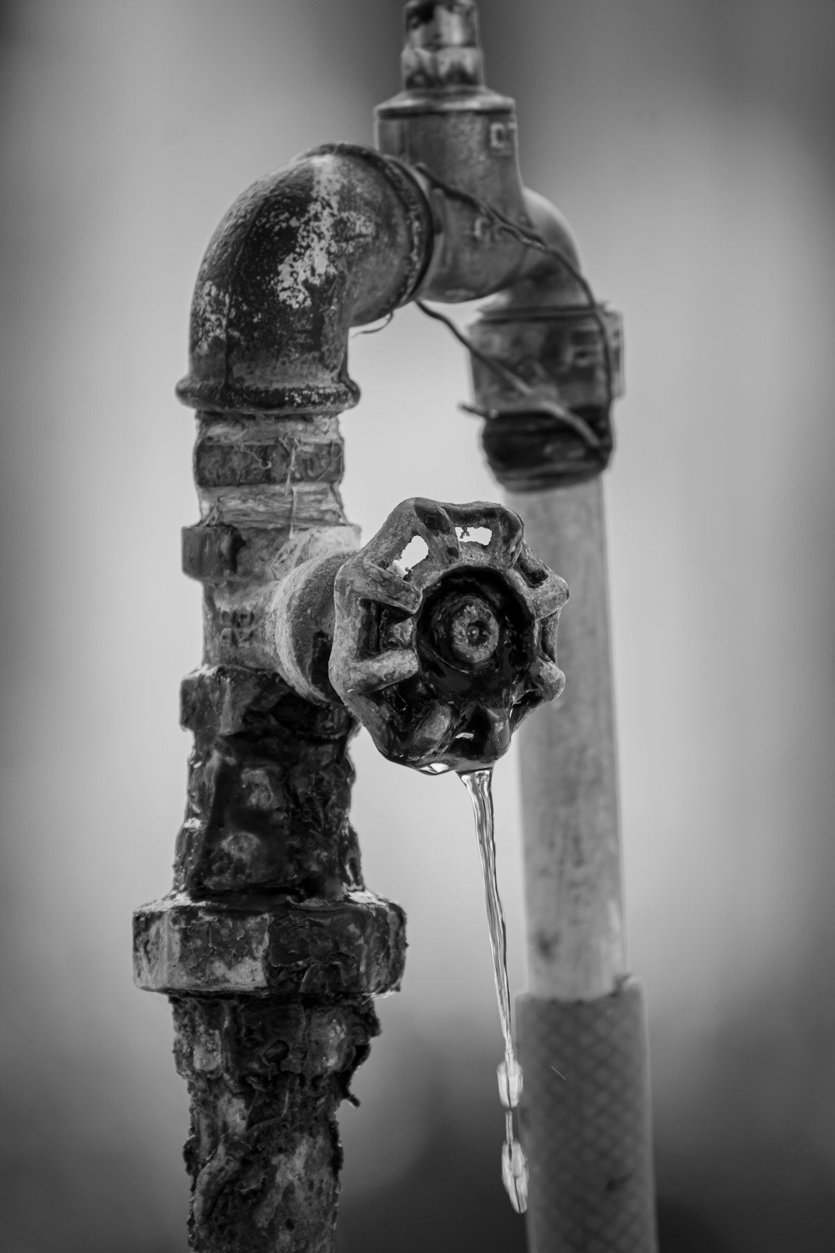 A worn faucet with a small water drop at the spout
