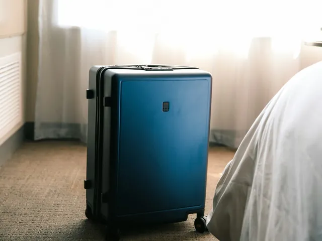 Blue suitcase standing beside a hotel bed