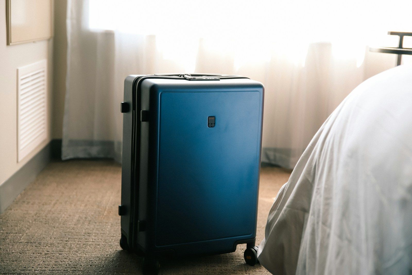 Maleta azul colocada junto a la cama de una habitación de hotel