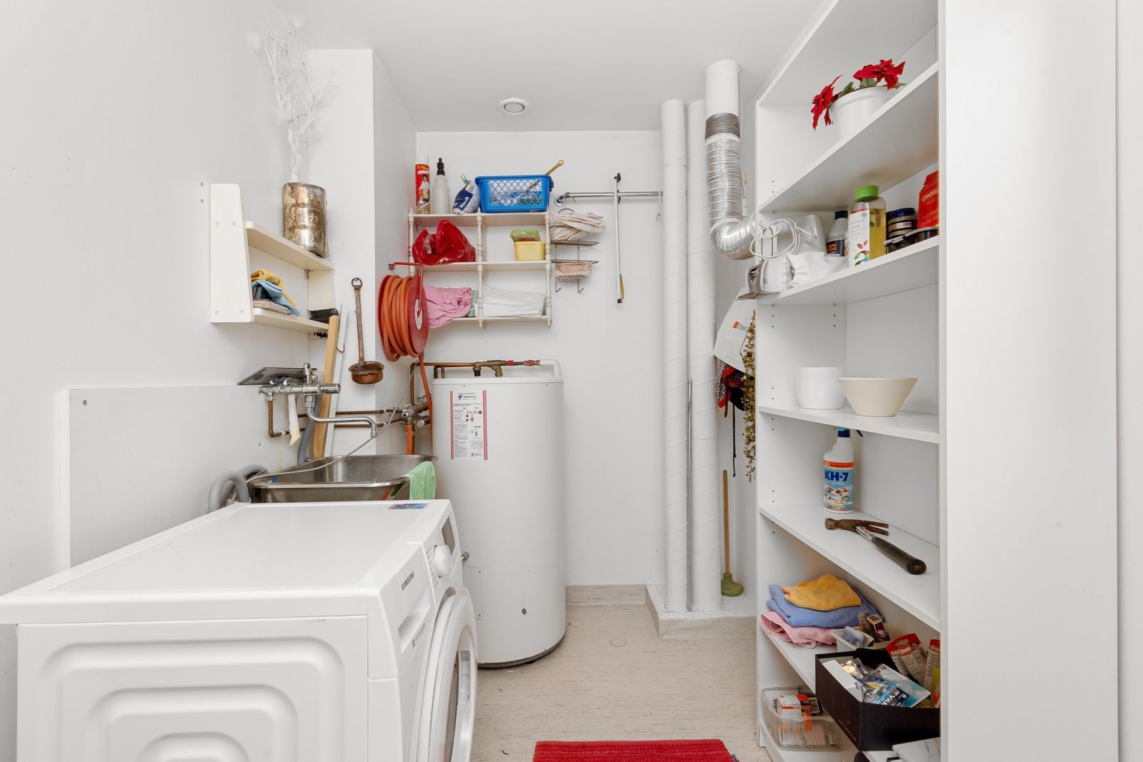Laundry room with a white water heater, washing machine and shelves