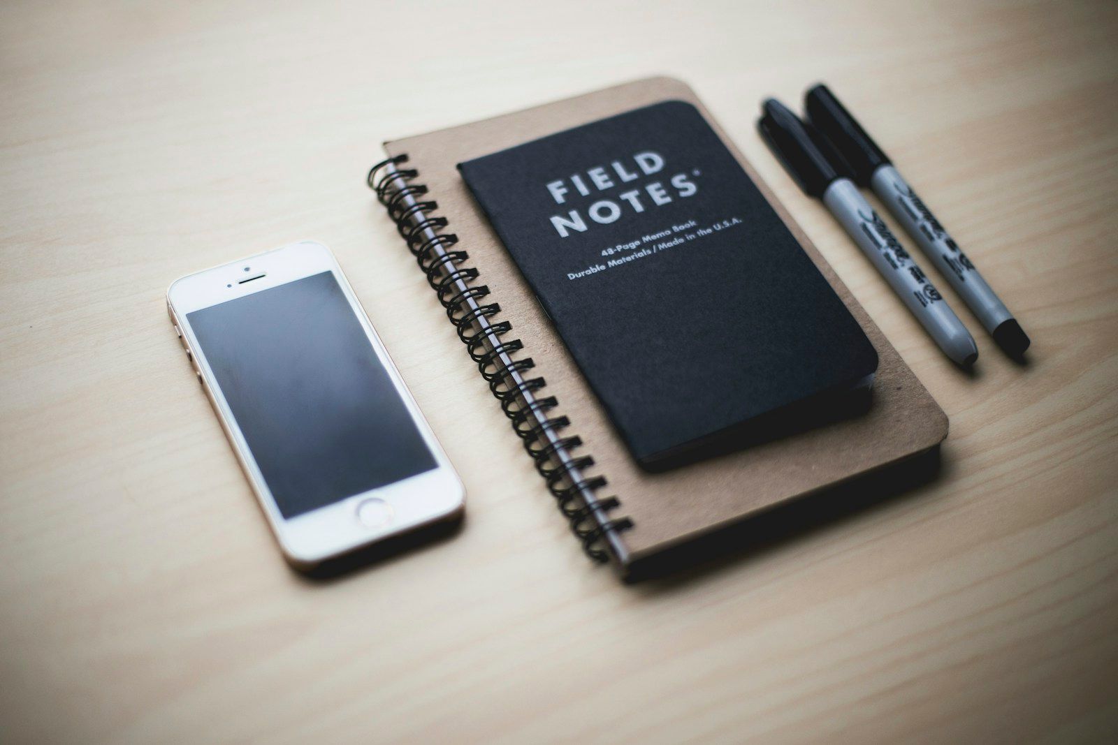 Smartphone beside a black notebook and pens on a wooden table